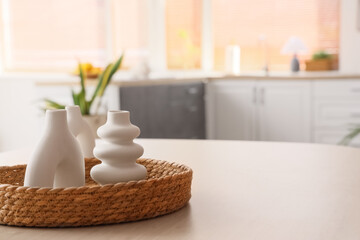 Wicker basket with decorative vases on wooden dining table in kitchen, closeup