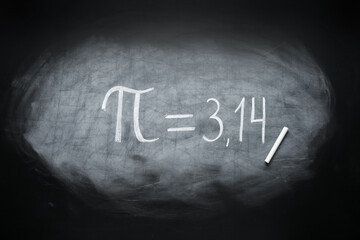 Number Pi written on black chalkboard with chalk in classroom