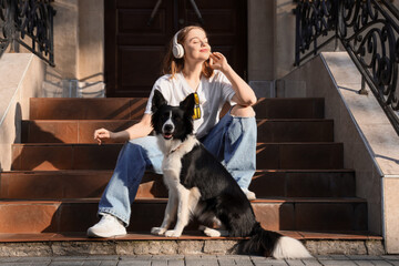 Pretty young woman in headphones and cute Border Collie dog sitting on stairs outdoors