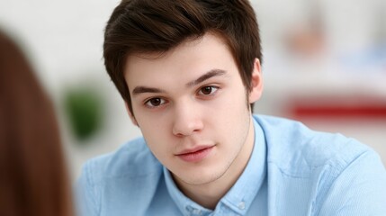 Young man with brown hair wearing a light blue collared shirt looks intently