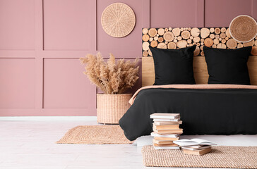 Interior of modern bedroom with cozy bed, black bedclothes, books and pampas grass near brown wall