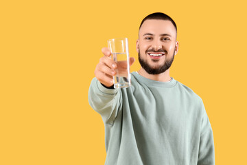 Young man with glass of water on yellow background