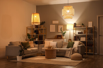 Interior of stylish living room with grey sofas, glowing lamps and bookshelves at evening