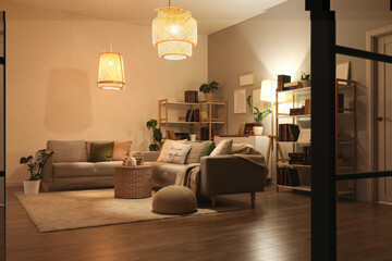 Interior of stylish living room with grey sofas, glowing lamps and bookshelves at evening