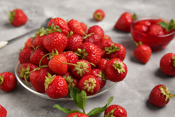Glass plate with sweet ripe strawberries and mint leaves on grey background, closeup