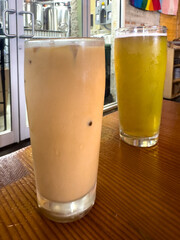 Two tall cold refreshments on a wooden bar. A light golden IPA pint glass with cling around the top...