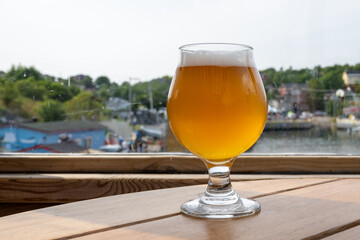 A tulip-shaped clear beer glass filled with a cold blonde ale on a wooden table. The booze has a...