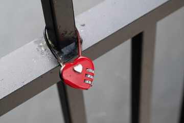 A bright red metal three digit combination lock on a metal railing of a fence. The symbolic gesture...