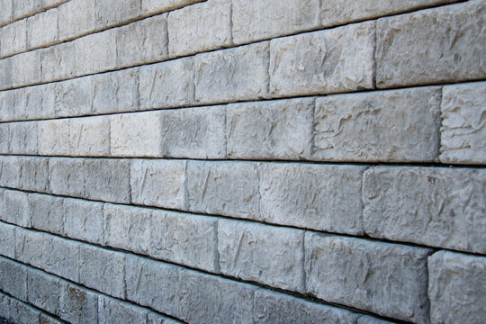 A large grey precast concrete block wall. The massive rectangle shaped bricks are interlocking cinder bricks with granular backfill. The textured castle style wall has large square caps.  - Powered by Adobe