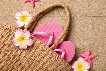 Obraz na płótnie Canvas Beach bag with plumeria flowers, starfishes and flip-flops on sand, top view