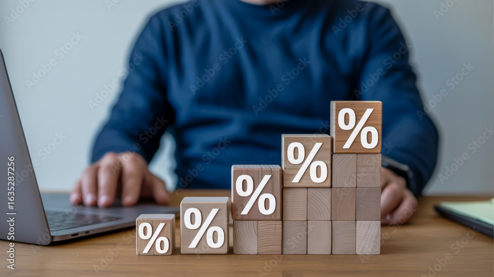 Poster wooden blocks with percentage symbols stacked in ascending order on a desk next to a laptop with a p