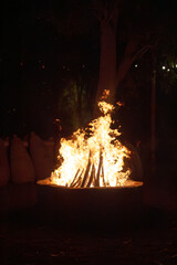 Campfire blaze with red and orange flames lighting the night. Heat radiates from the wood as smoke...