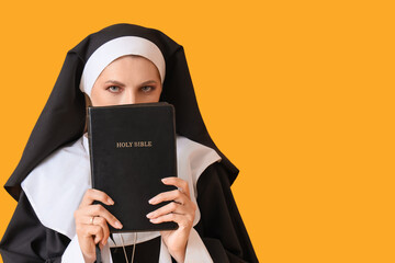 Mature woman dressed as nun with Holy Bible on yellow background. Halloween celebration
