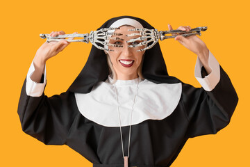 Happy mature woman dressed as nun with skeleton hands on yellow background. Halloween celebration
