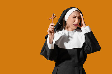 Disgusted mature woman dressed as nun with wooden cross on yellow background. Halloween celebration