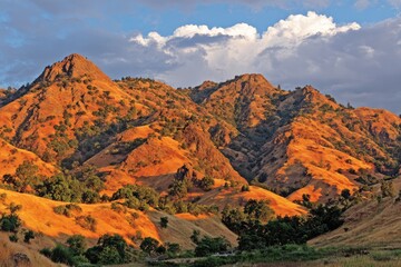 Golden hills, rugged peaks, dramatic cloudscape