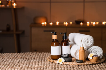 Beautiful composition with towels, cosmetic products, flowers, sea salt and spa stones on wicker table in dark salon