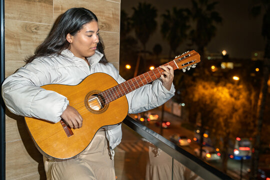 Singer songwriter composing new music playing acoustic guitar at night on balcony