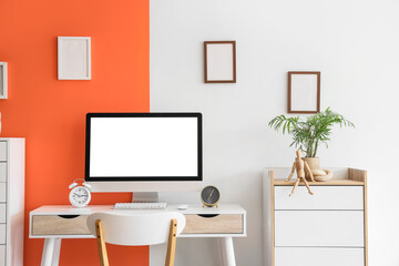 Fototapeta premium Comfortable workspace with modern computer, alarm clocks and houseplant near color wall
