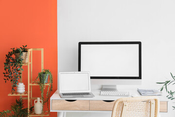 Comfortable workspace with modern computer, laptop and houseplants near color wall, closeup