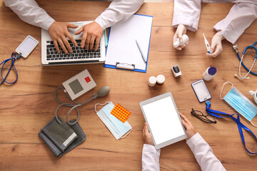Doctors with tablet computer, laptop and medicine working at wooden table, top view