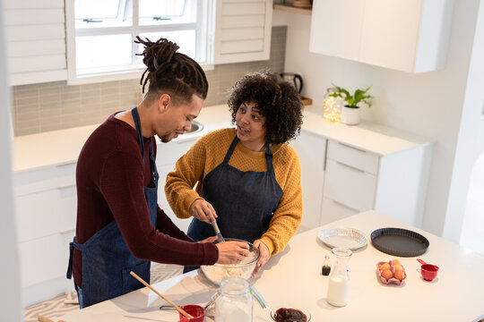 African American couple wearing denim aprons mixing batter at kitchen island with whisk and spatula