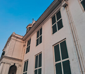 Fatahillah Museum or Jakarta History Museum facade in Kota Tua with colonial architecture, green wooden shutters, and white walls under blue sky