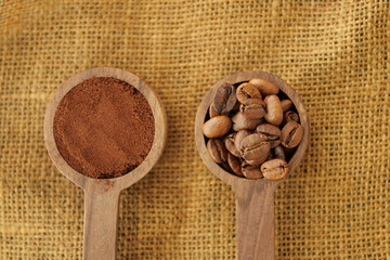 Ground coffee and whole beans in wooden spoons on burlap