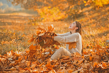 Girl in autumn orange leaves. Yellow fallen maple leaf holds a female hand in the park. Portrait of...