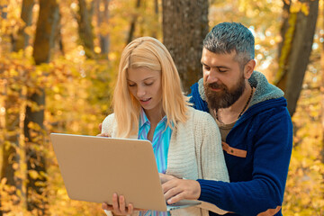 Naklejka premium Business couple, man and woman using laptop in Autumn fall nature park. Business outdoor in autumn park. Couple in Autumn fall park. Man and woman near Autumn fall leaves.