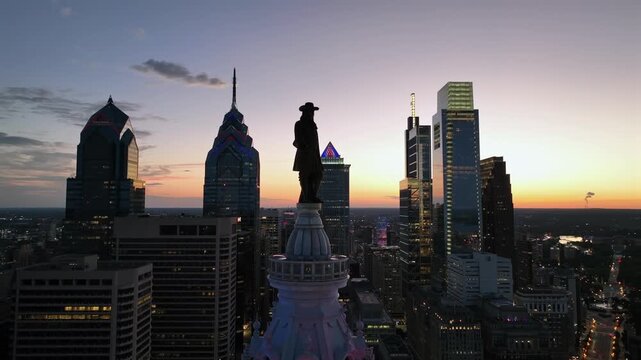 William Penn statue on top of city hall tower in Philadelphia city. Aerial rising wide shot. Cozy sunset time. One liberty place and comcast technology center in background. Night scene. PA, USA
