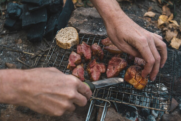 hands skillfully prepare marinated meat on grill above glowing embers. surrounding leaves turn...