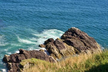 Rocky coastline with waves crashing against the shore under a clear blue sky.