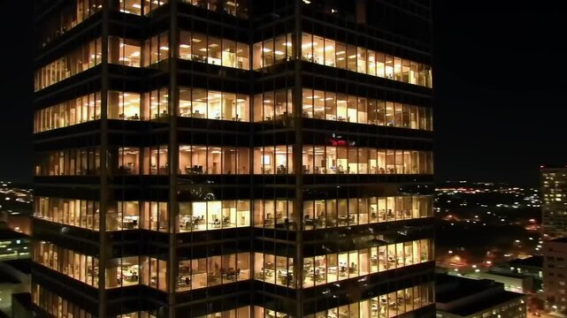 Nighttime view of a modern office building with illuminated windows and city skyline