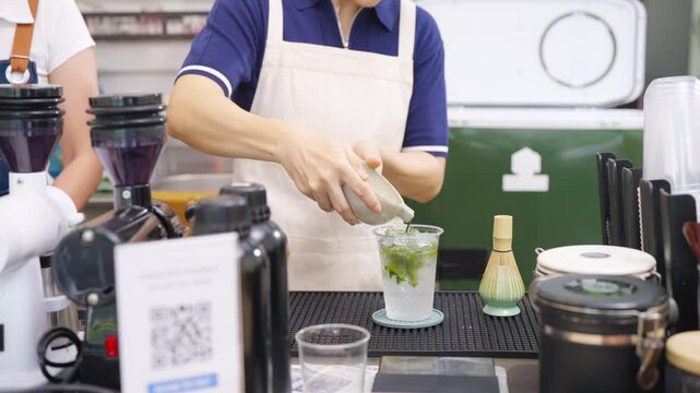 Small business entrepreneur coffee shop cafe accepts payment via QR code. Barista preparing iced green tea on bar counter. Non binary person working part time job serving beverage drink to customer.