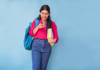 Young asian indian teenager student girl using smart phone and books isolated on blue background....