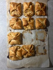 Freshly baked puff pastry pies with cheese filling on parchment paper top view. 
