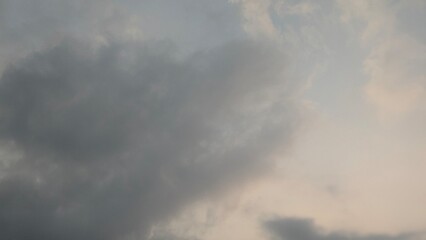 A vertical view of a cloudy sky with soft, diffused light. The thick gray and white clouds, with a...