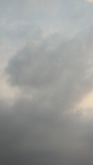 A vertical shot of a dark, overcast sky. The image shows thick gray clouds with a hint of light on...
