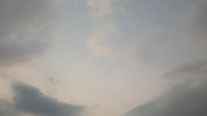 A vertical view of a cloudy sky with soft, diffused light. The thick gray and white clouds create a...
