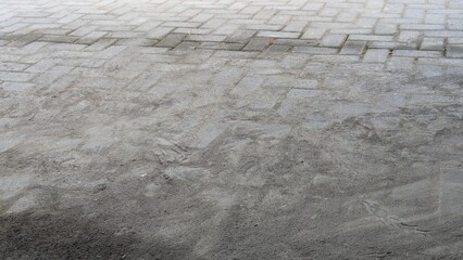 An overhead view of a gray paver block surface. The top half shows a clean herringbone pattern,...