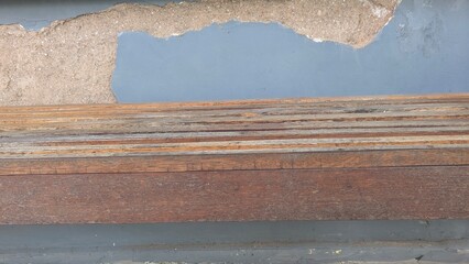 A close-up of a stack of weathered wooden planks against a peeling, painted wall. The rustic...
