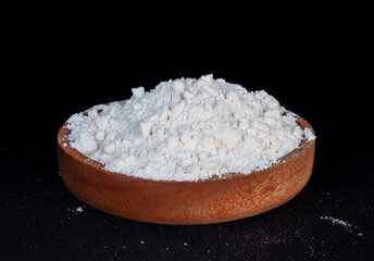 flour in a wooden plate on black background
