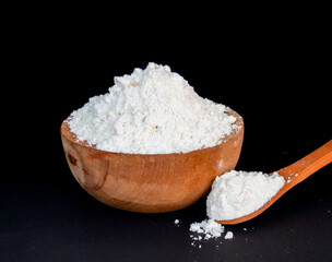 wooden spoon and bowl with white rice flour on a black background