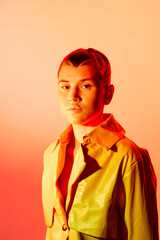 woman with short hair wearing glossy yellow jacket looking serious, vibrant warm lighting, stylish...