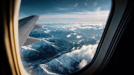 Airplane wing above snow capped mountains and clouds viewed through aircraft window