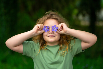 Spring flowers near child face. Kid in blooming spring garden. Child face close-up, covering eyes...