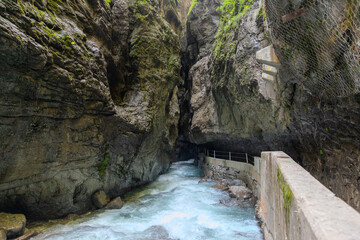 Narrow walkway carved into the cliffside along a turquoise stream inside Partnachklamm Gorge,...
