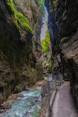 Narrow walkway carved into the cliffside along a turquoise stream inside Partnachklamm Gorge,...