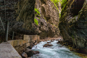 Narrow walkway carved into the cliffside along a turquoise stream inside Partnachklamm Gorge,...